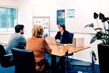 Afbeelding van arts met patient en begeleider aan tafel