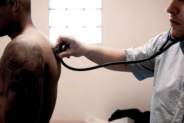 Foto van een arts die een patient op de rug beluistert met een stethoscoop