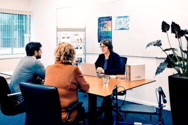 Afbeelding van arts met patient en begeleider aan tafel