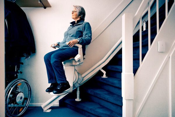 Vrouw zit op een traplift, die onder aan de trap staat.