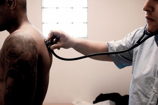 Foto van een arts die een patient op de rug beluistert met een stethoscoop