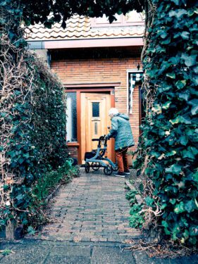 Foto van oudere dame met rollator voor voordeur.