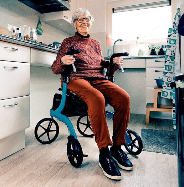 oudere vrouw zit in de keuken op een rollator