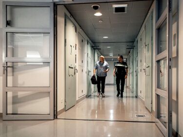 Foto van huisarts en politieagent die door een gang van arrestantencomplex lopen