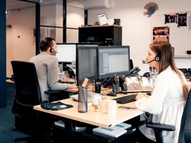 Foto van het medTadvies secretariaat, waar 2 mensen aan het werk zijn achter computer en headset op